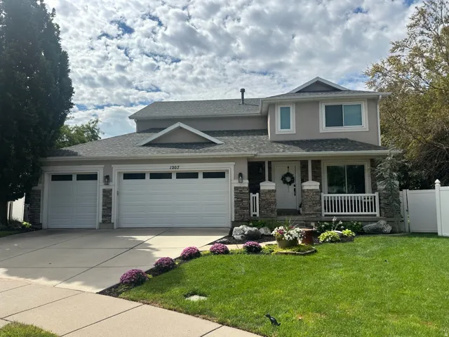 Two-story stucco exterior with stone accents, a three-car garage, and a covered front porch featuring white railings