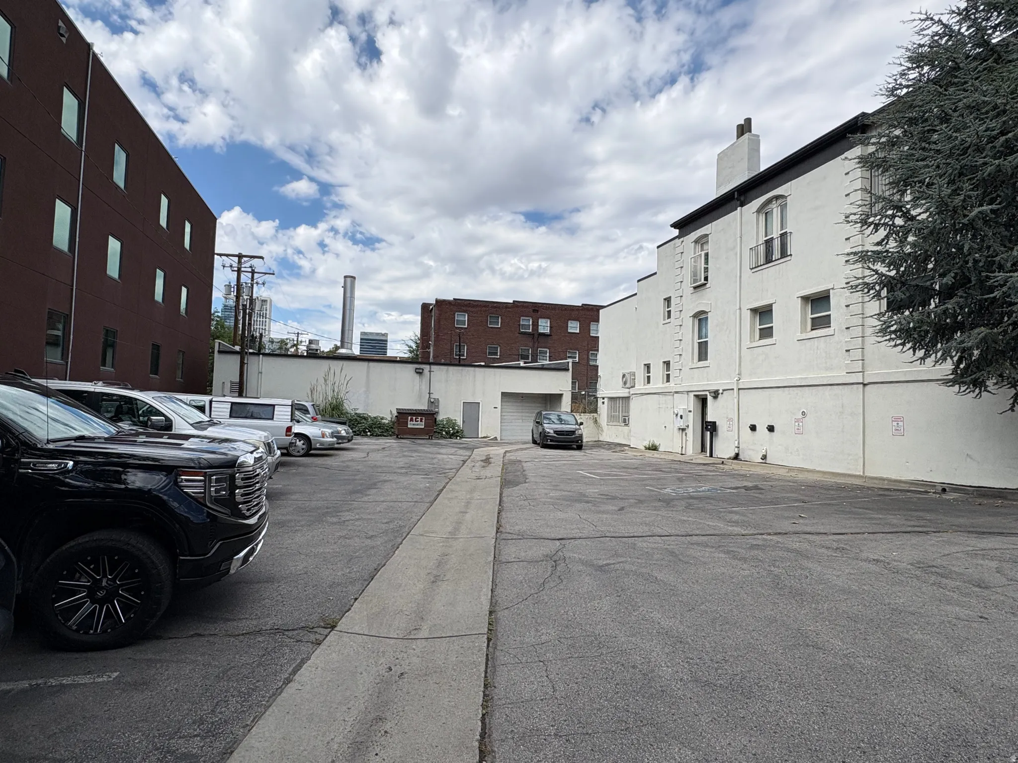 Paved parking lot with a concrete curb and adjacent white building featuring multiple windows and a chimney