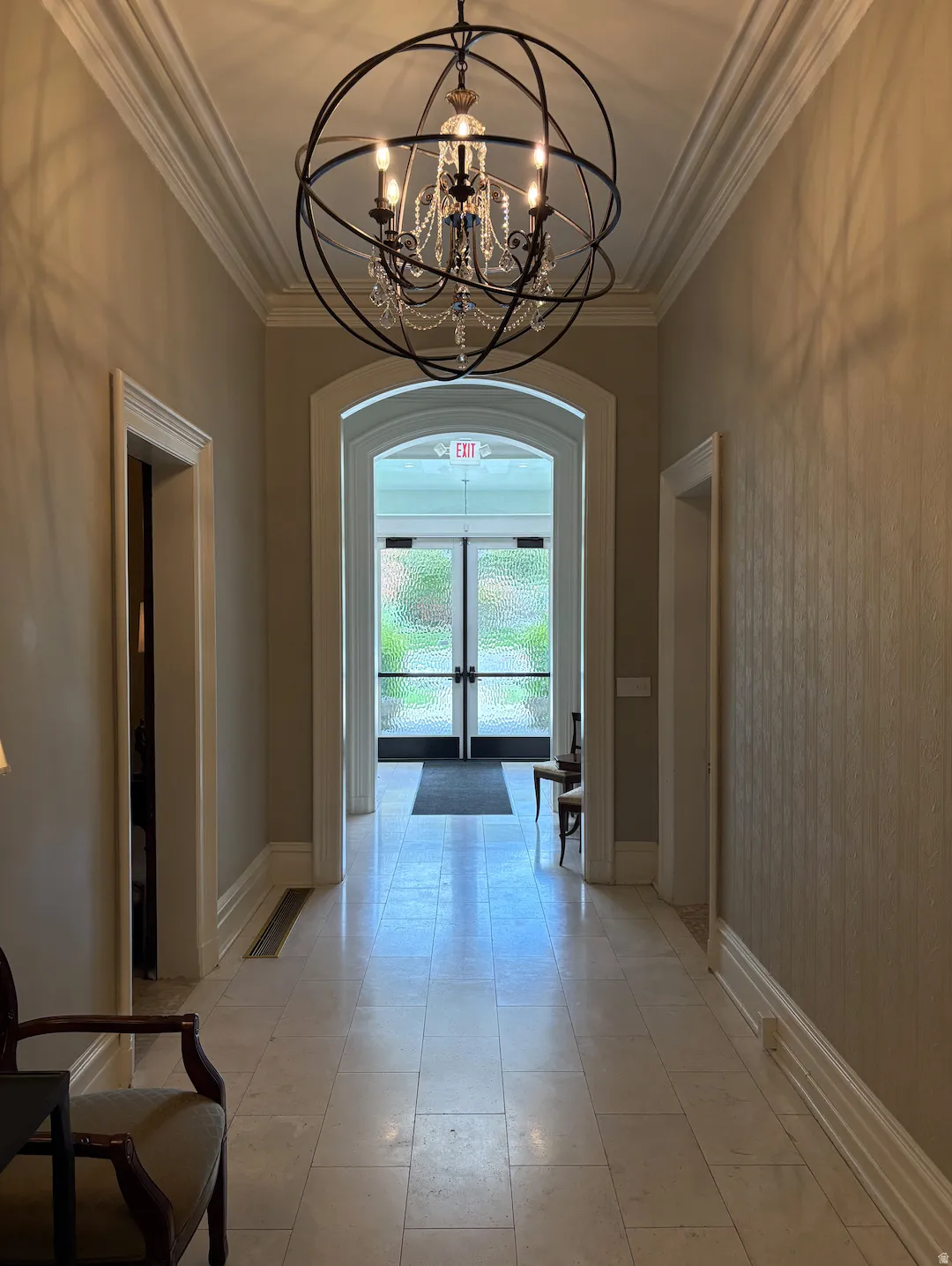 Hallway featuring a decorative chandelier, crown molding, arched doorways, and tile flooring
