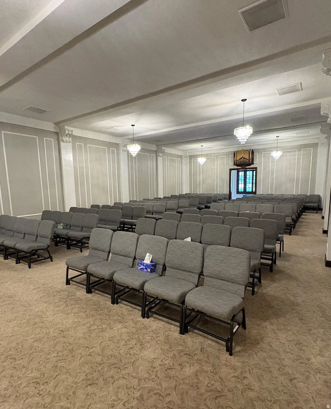 Spacious room featuring multiple rows of seating, patterned carpeting, decorative wall paneling, and multiple chandeliers