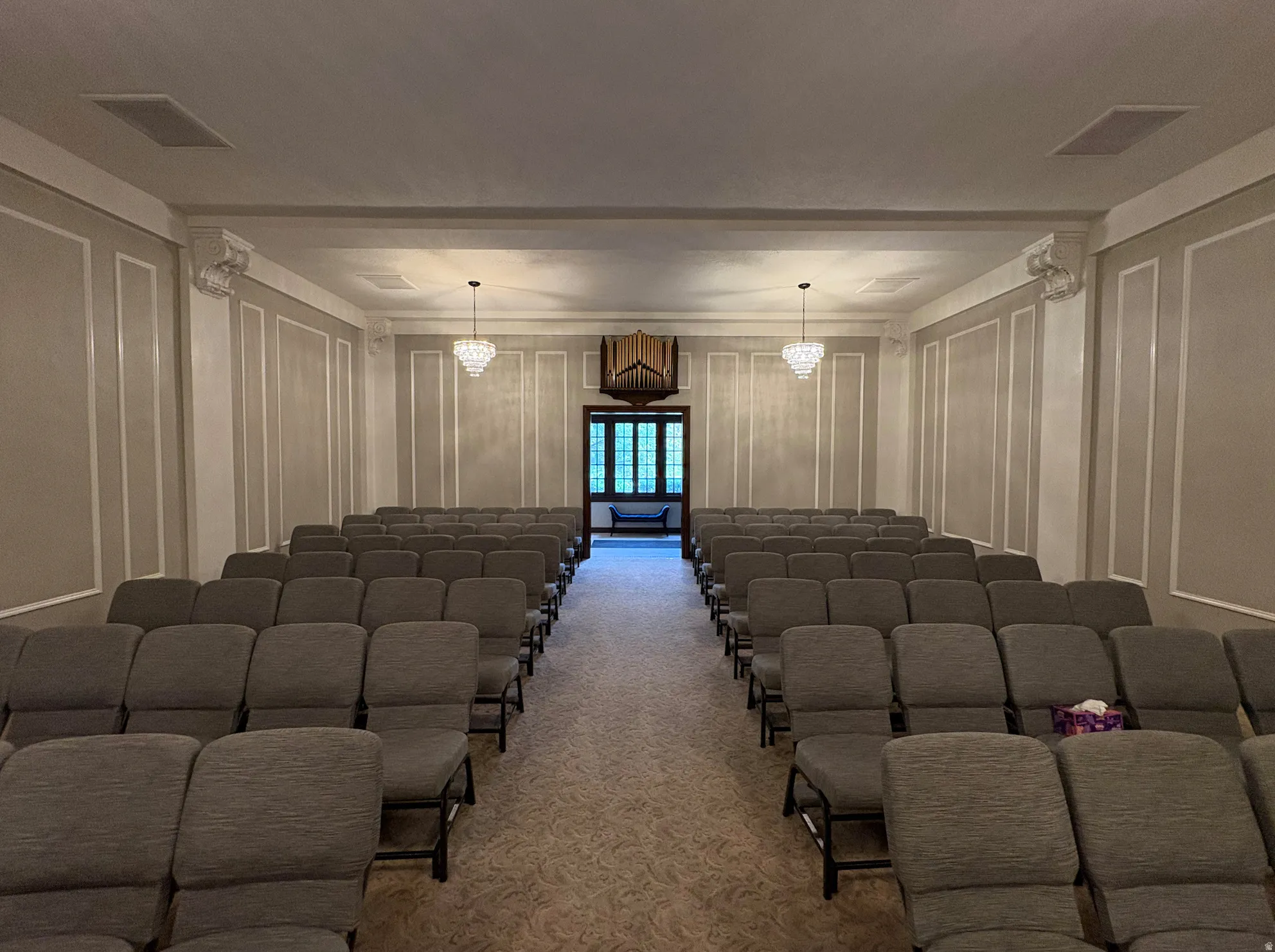 Decorative wall paneling, dual crystal chandeliers, recessed ceiling speakers, patterned carpeting, and a built-in pipe organ