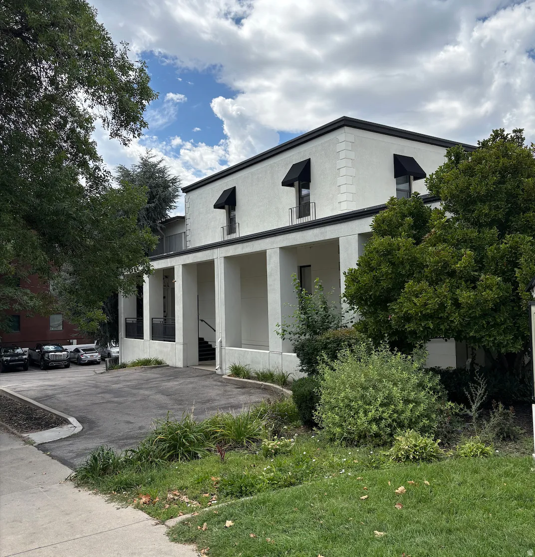 Stucco exterior with black awnings, black trim, and a paved parking area