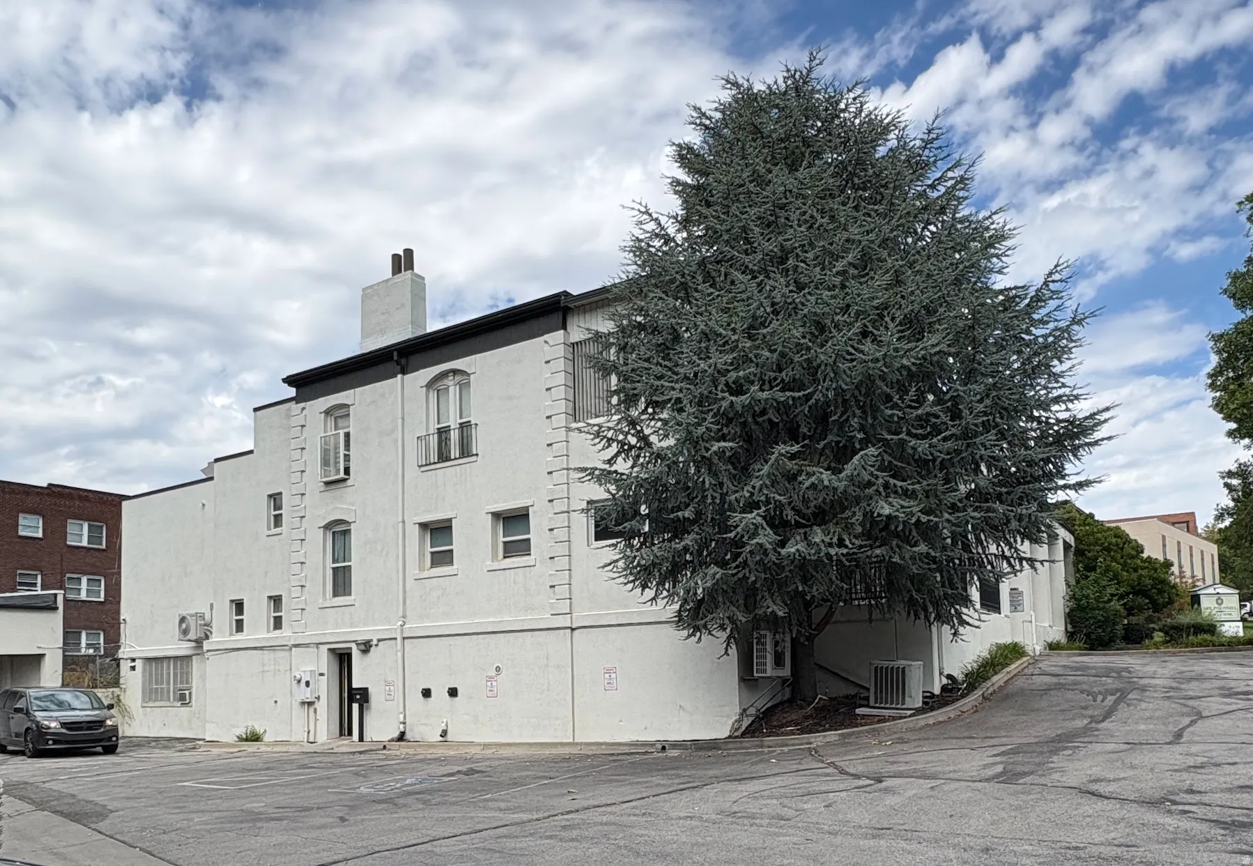 White exterior with a dark trim, featuring multiple windows and a mature evergreen tree