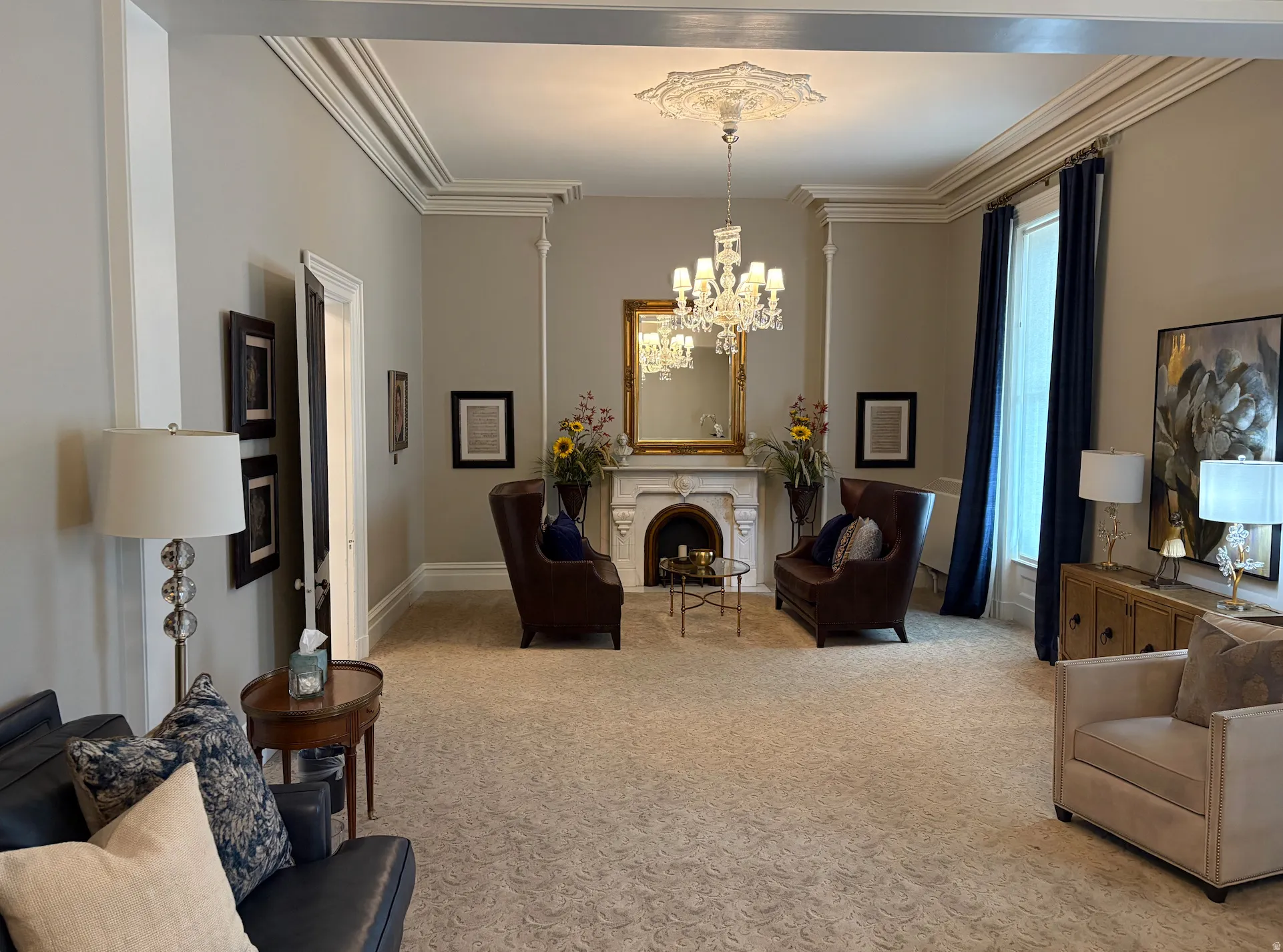 Formal living space featuring crown molding, an ornate ceiling medallion, a crystal chandelier, a decorative fireplace with a mantel, and a large window
