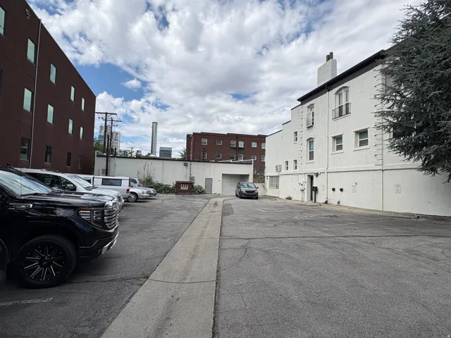 Paved parking lot with a concrete curb and adjacent white building featuring multiple windows and a chimney