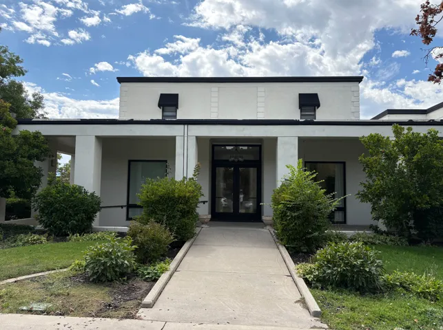 Contemporary building exterior featuring a central entrance with double doors, symmetrical windows with black awnings, and a concrete pathway