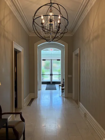 Hallway featuring a decorative chandelier, crown molding, arched doorways, and tile flooring