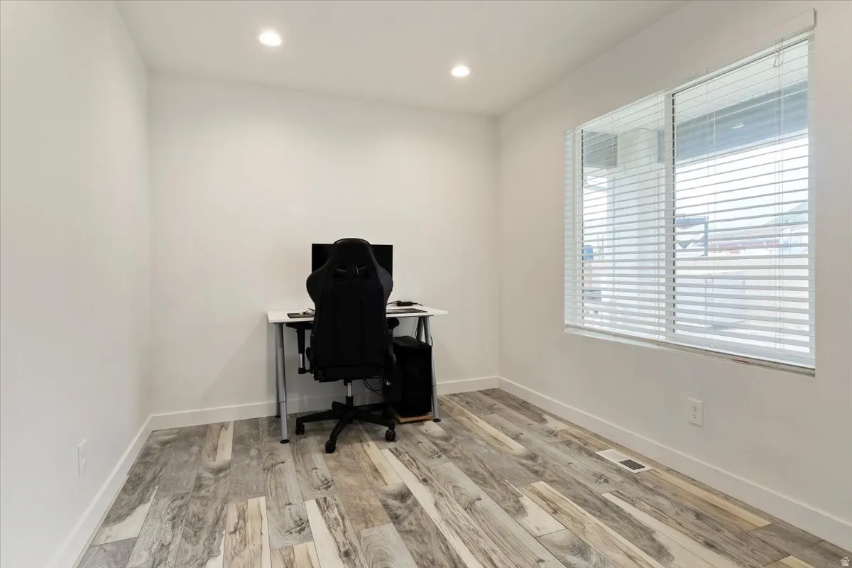 Recessed ceiling lighting, wood-finish flooring, white walls, and a large window with blinds