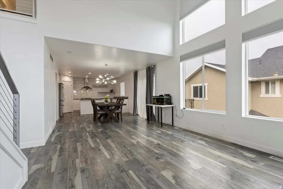 Spacious open-concept living area with high ceilings, large windows, wood-finish flooring, and a modern chandelier