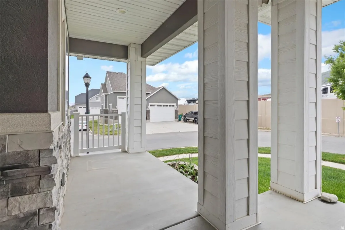 Covered porch featuring a concrete surface, white shingle-style columns, and a stacked stone wall accent