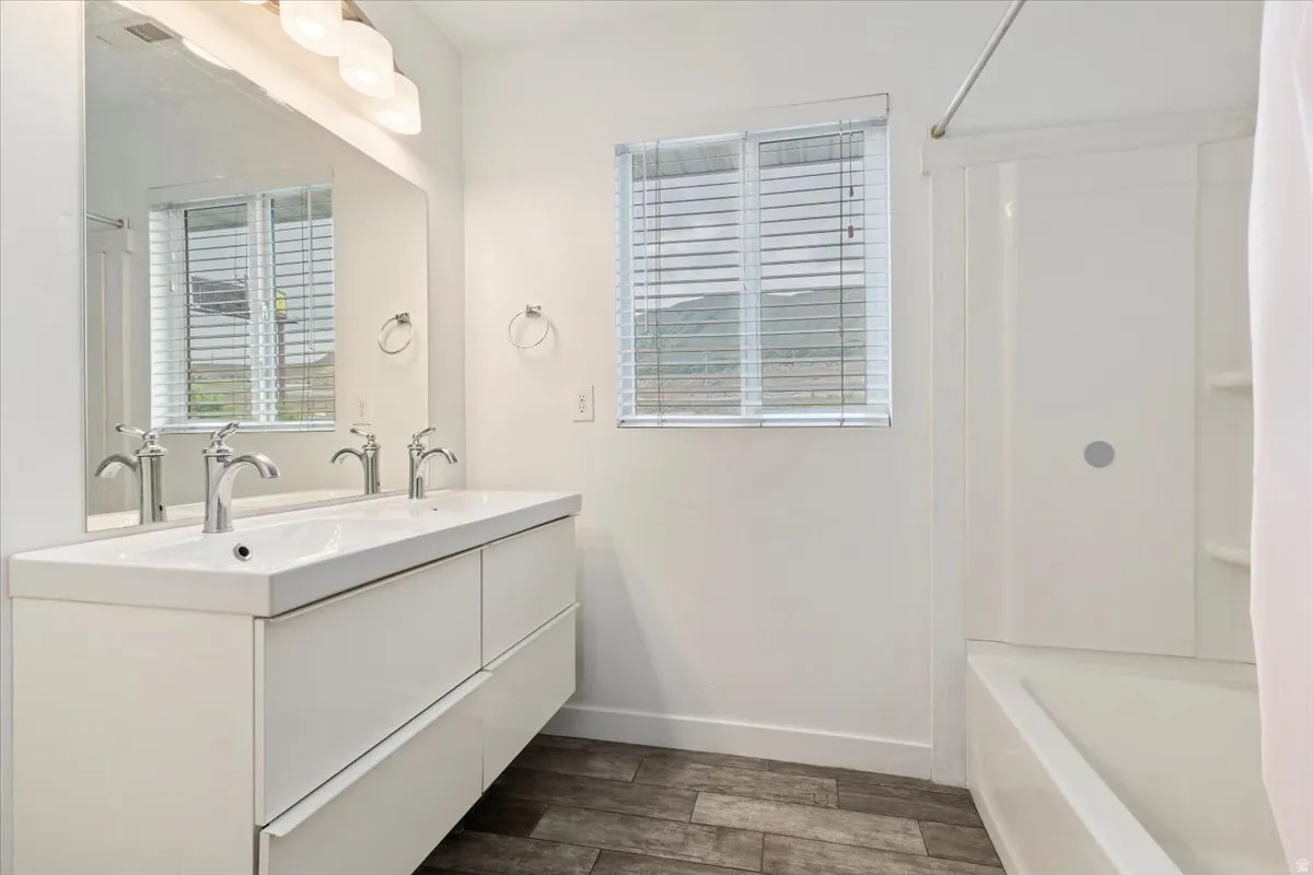 Dual sink vanity with white cabinetry, wood-finish flooring, and a white shower-over-tub combination