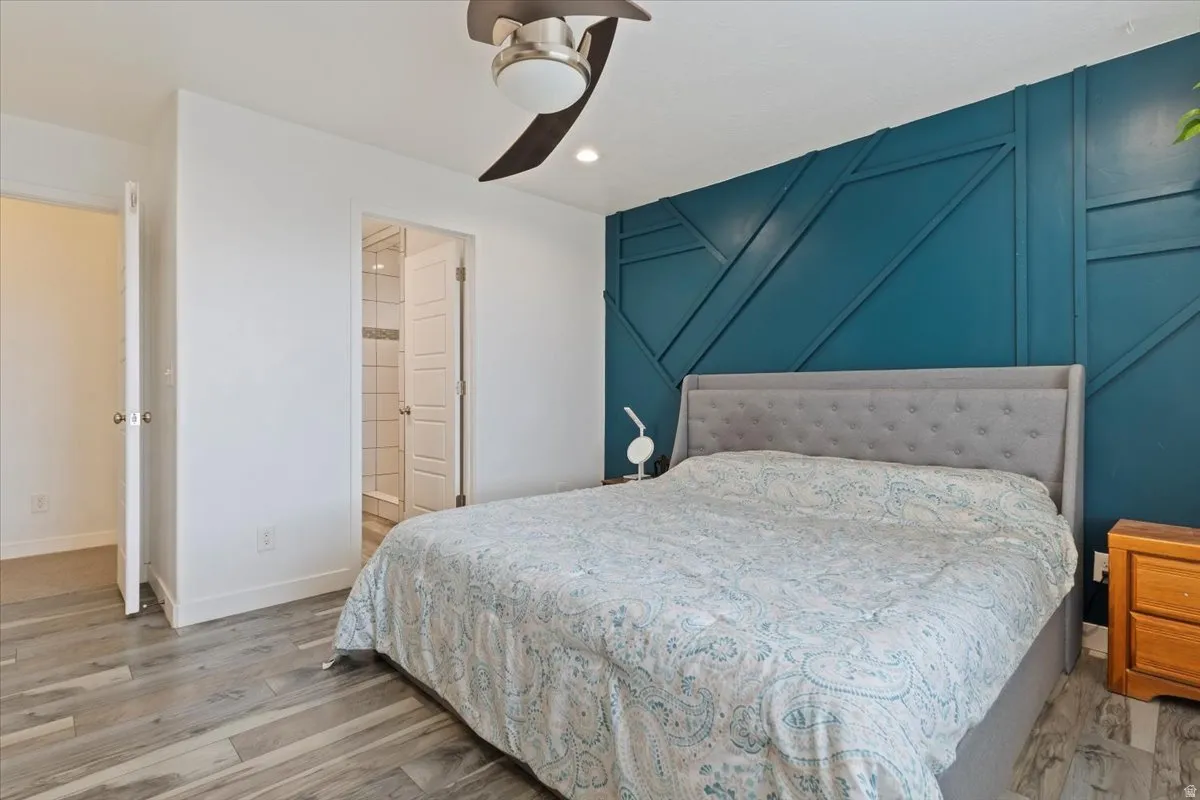 Wood-finish flooring, accent wall with geometric paneling, ceiling fan with integrated lighting, and a neutral color palette