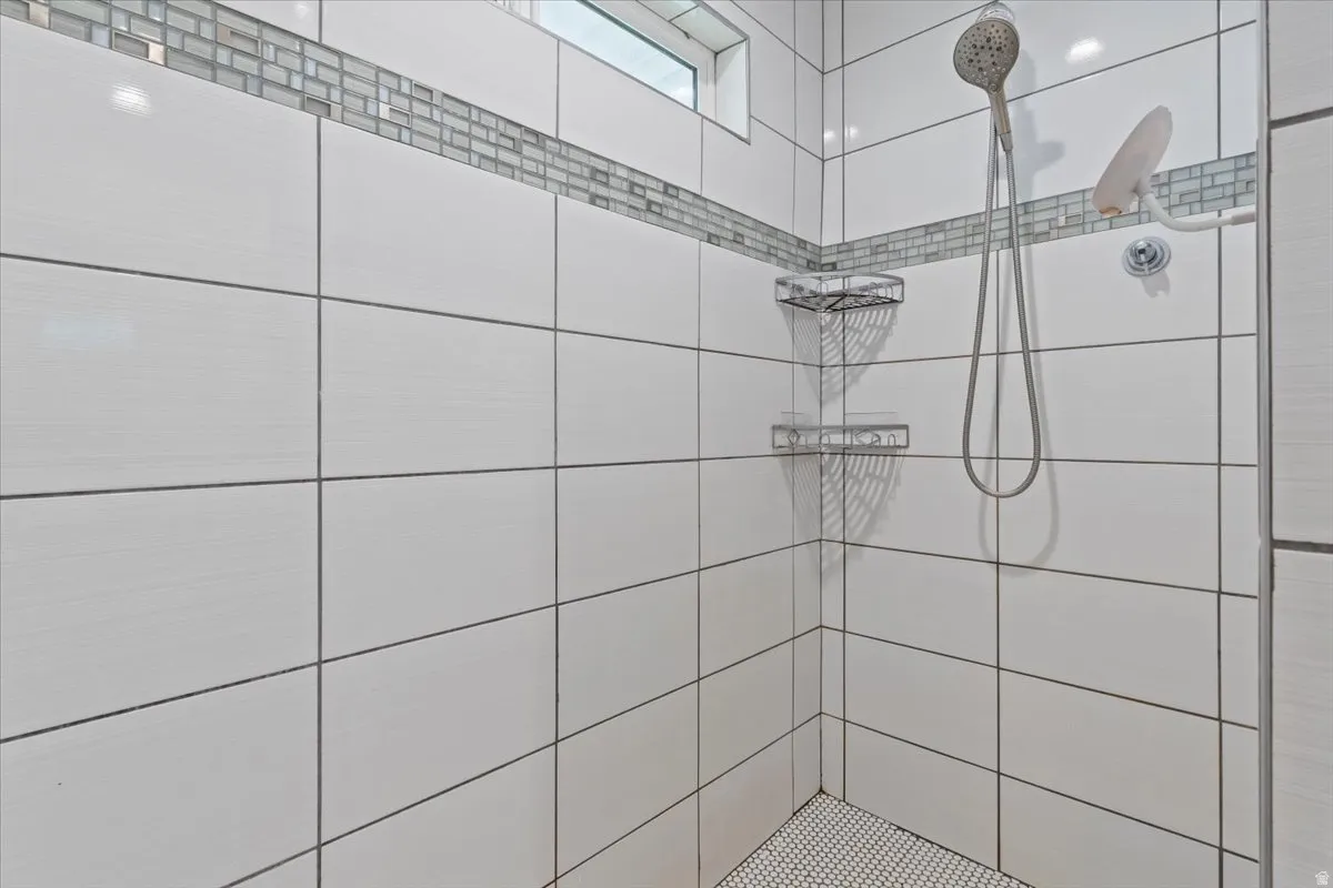 Shower featuring large format white wall tiles, an iridescent mosaic tile accent, a handheld showerhead, and built-in shelving