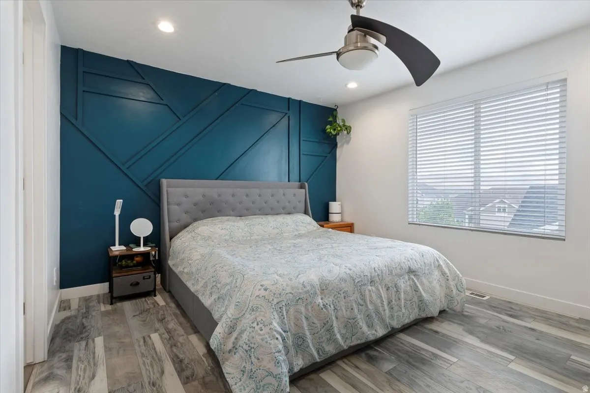 Feature wall with geometric molding, recessed lighting, wood-finish flooring, ceiling fan, and window with blinds
