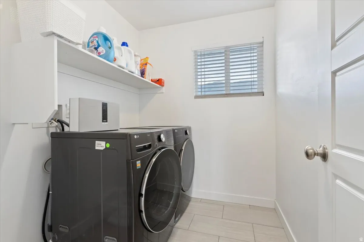 Laundry area featuring a window with blinds, white shelving, tile flooring, and a paneled door with a brushed nickel knob