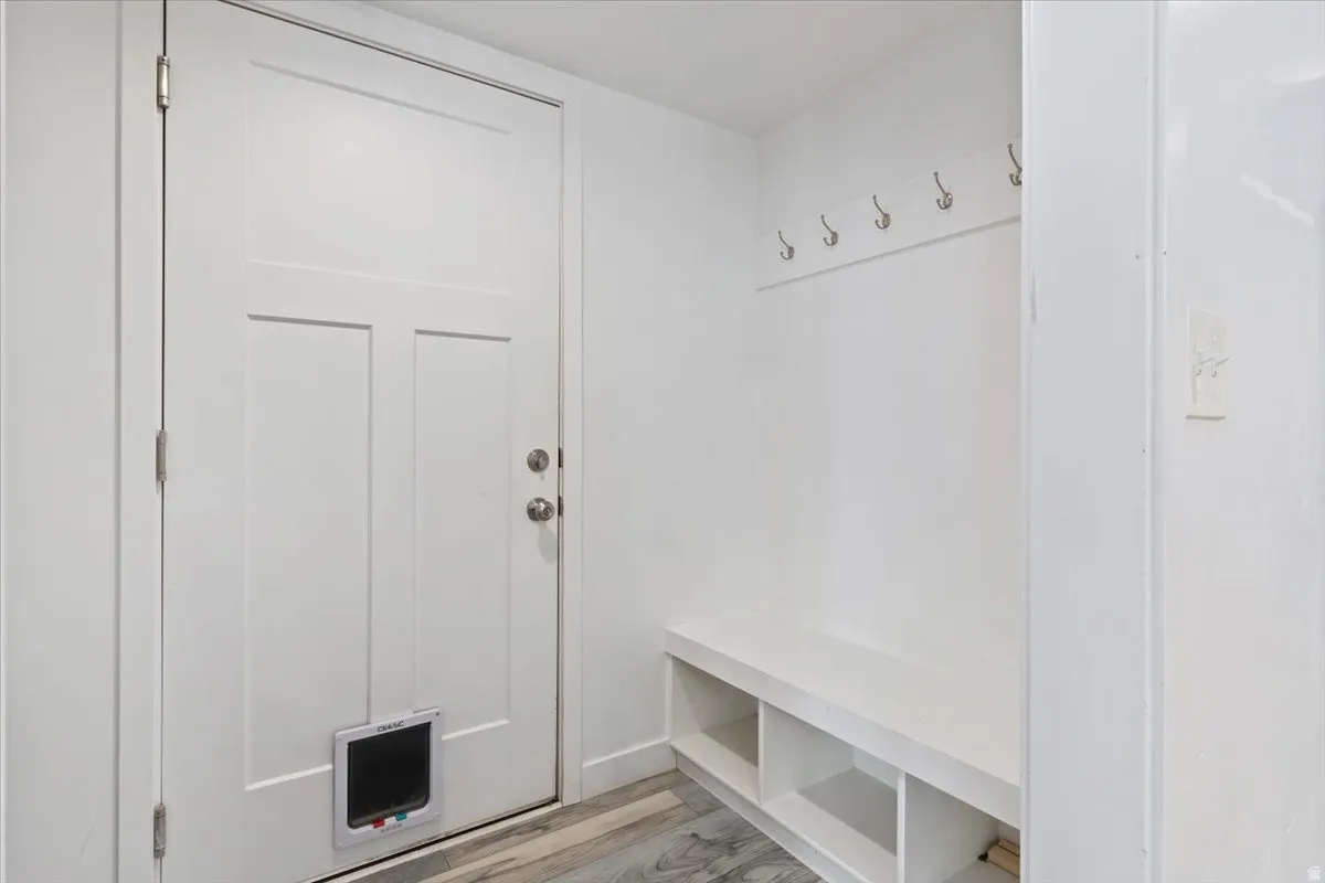 Entryway featuring wood-finish flooring, a solid panel door, and a built-in bench with storage cubbies and wall-mounted hooks