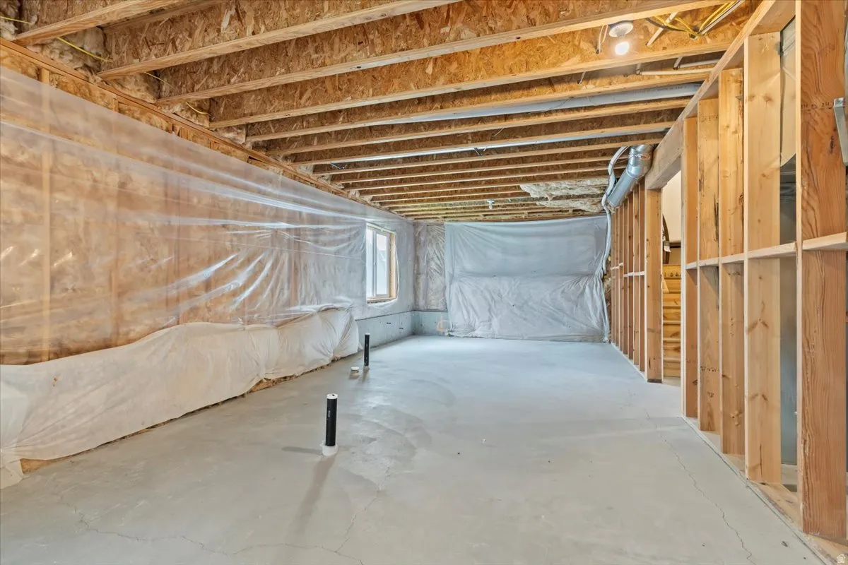 Unfinished basement featuring exposed wood joists, framed walls, and a concrete floor