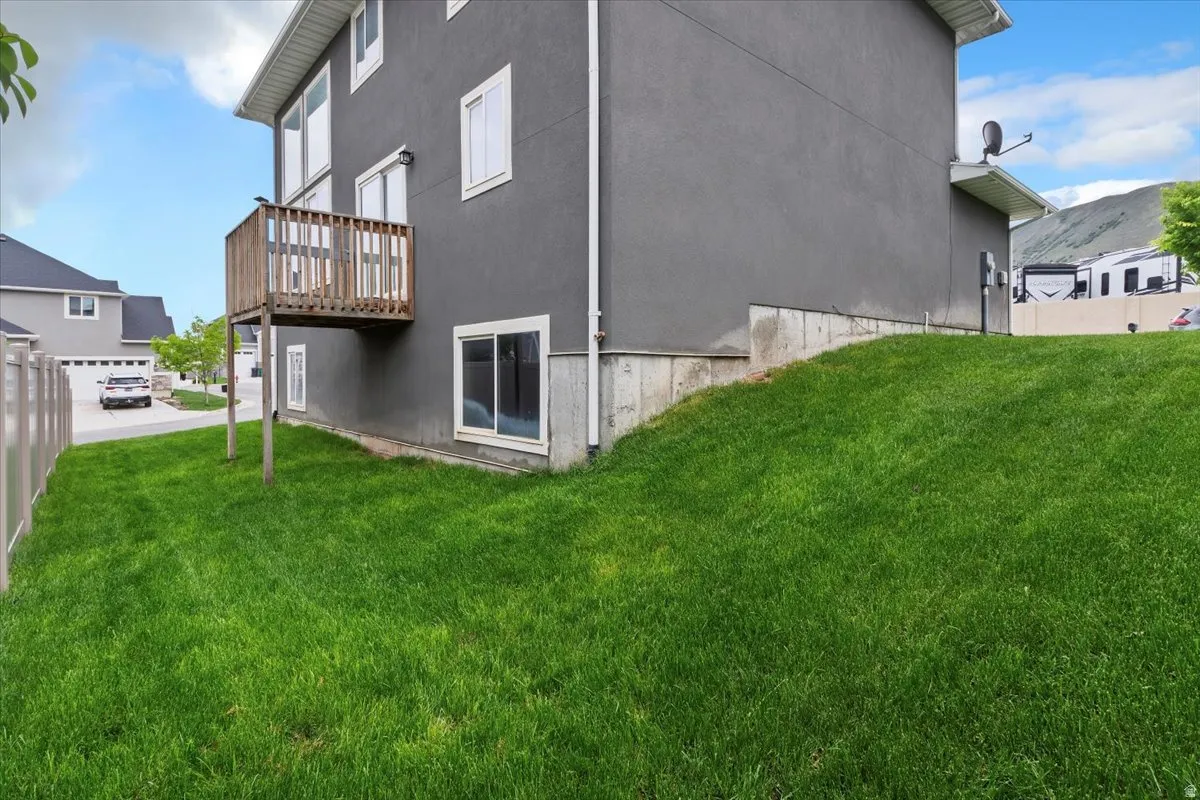 Gray stucco exterior with white-framed windows, a wood deck, and a sloped lawn