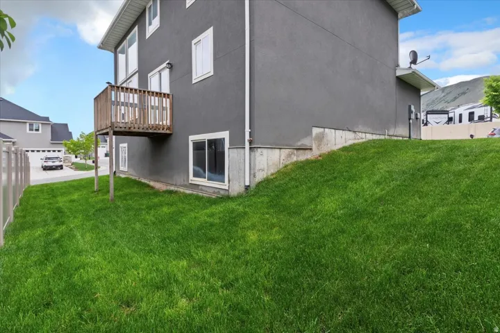 Gray stucco exterior with white-framed windows, a wood deck, and a sloped lawn