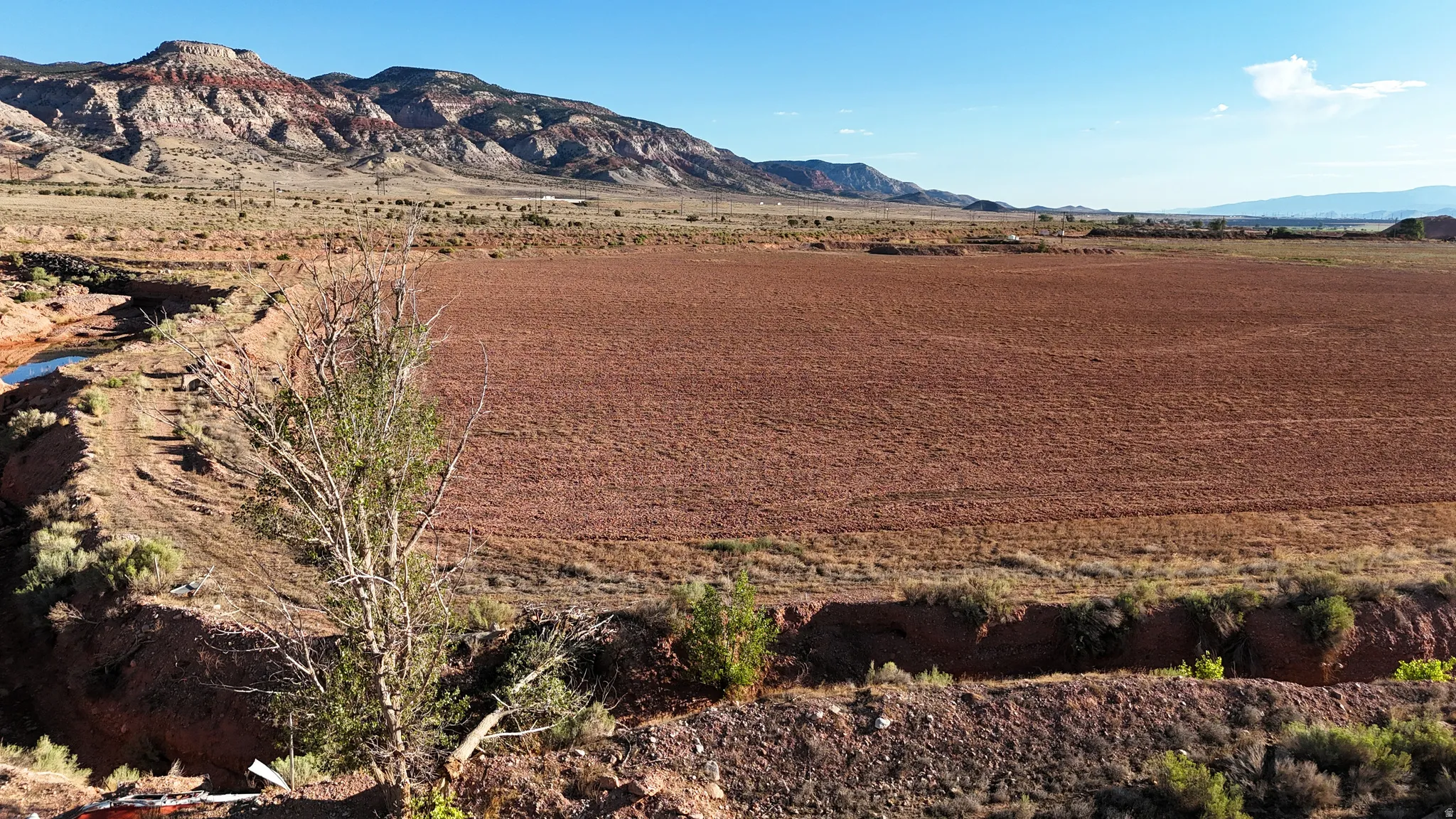 Expansive cleared land featuring rich red soil and a natural water channel