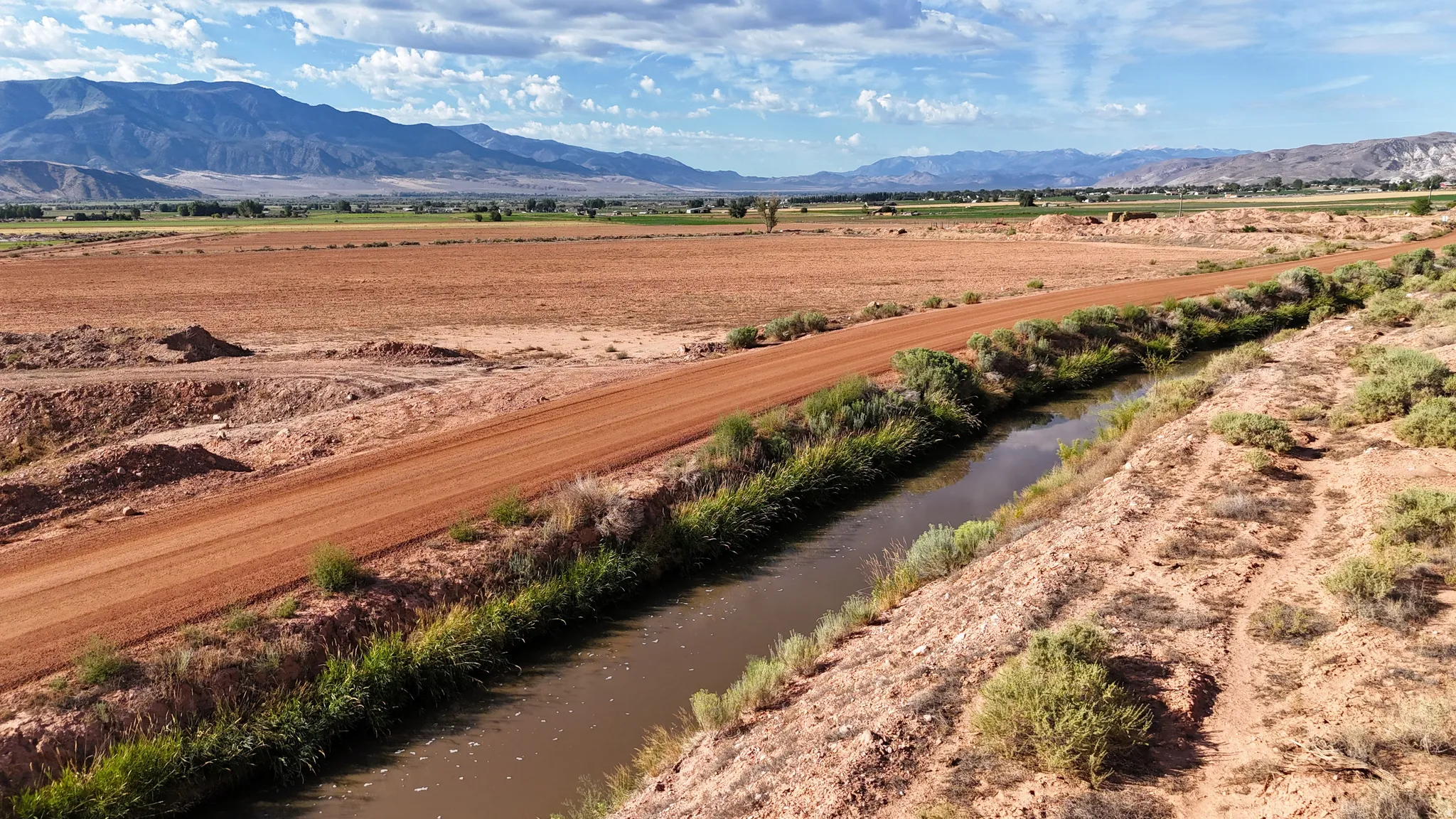 Expansive land parcel featuring a dirt road, natural water channel, and distant mountain range