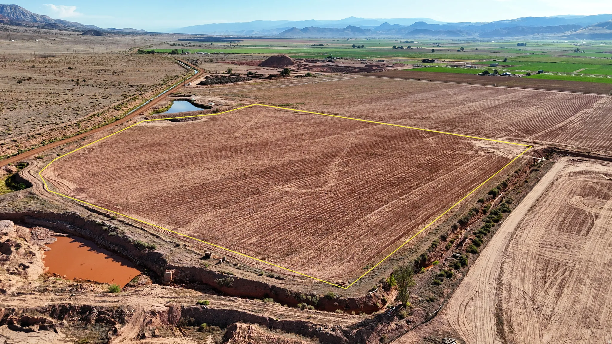 Expansive cultivated land featuring a defined perimeter, natural water features, and distant mountain ranges