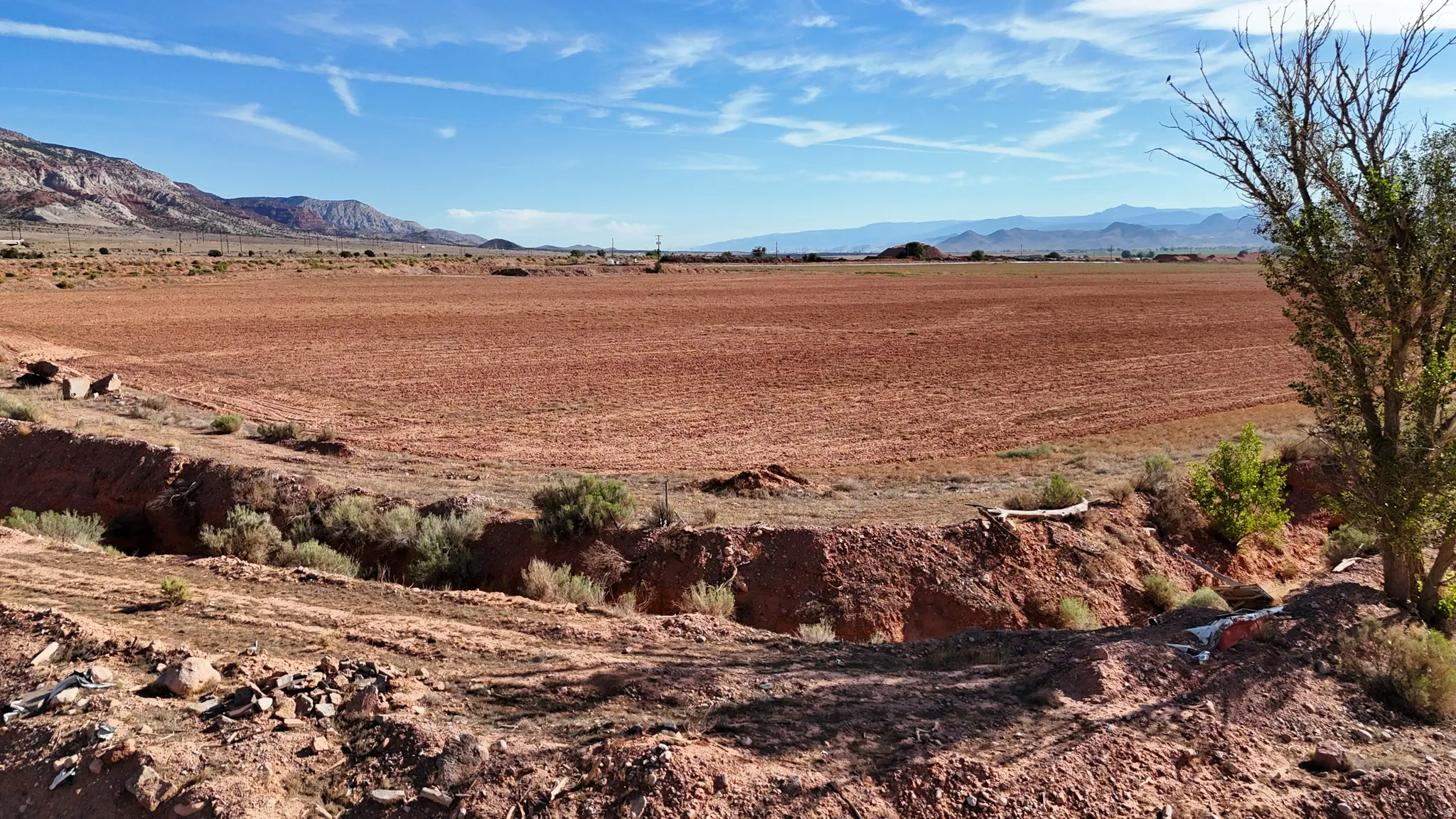 Expansive land parcel featuring exposed red earth and distant mountain formations under a broad sky