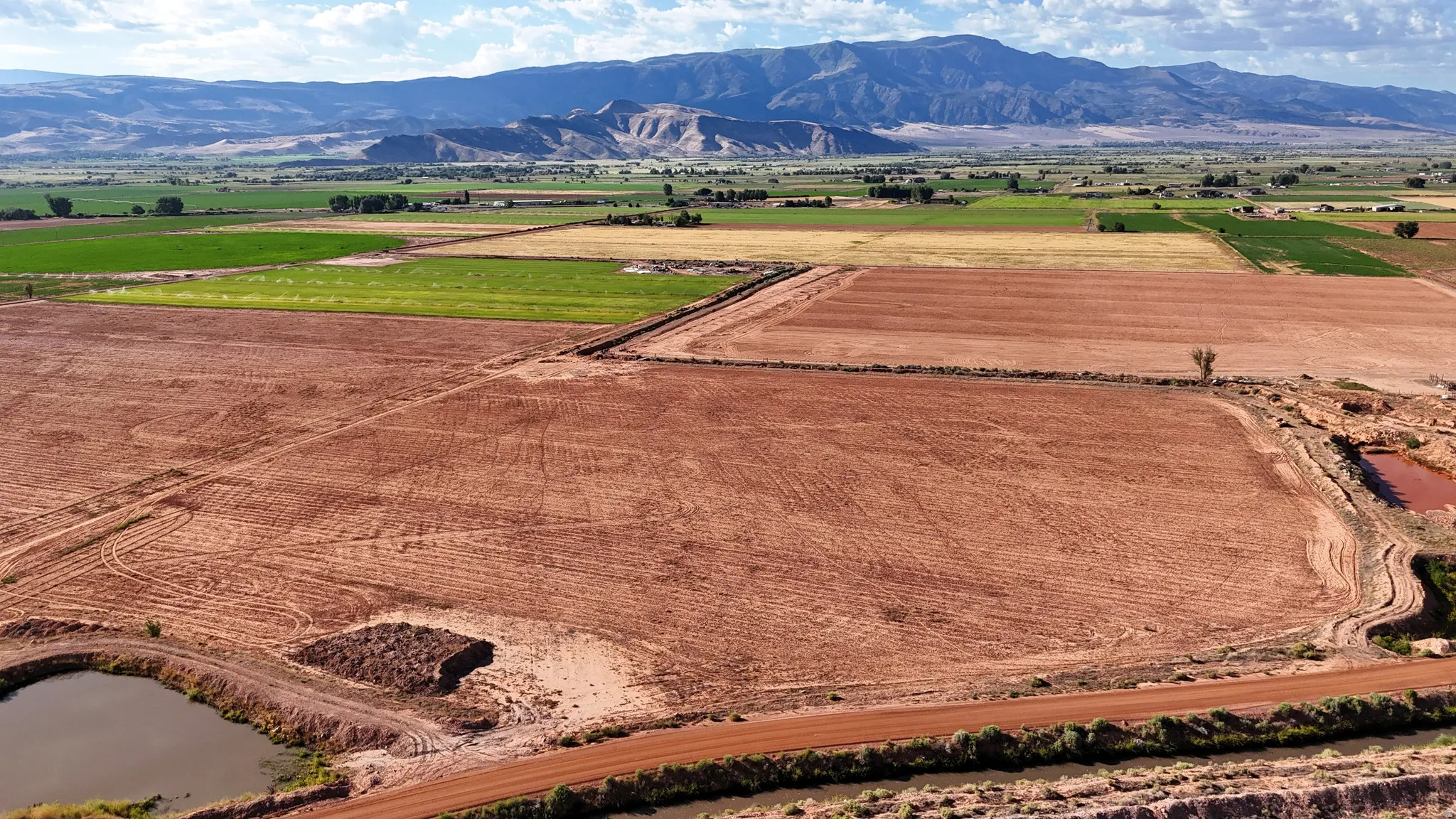 Expansive agricultural land featuring cultivated fields, a tranquil pond, and a mountainous backdrop