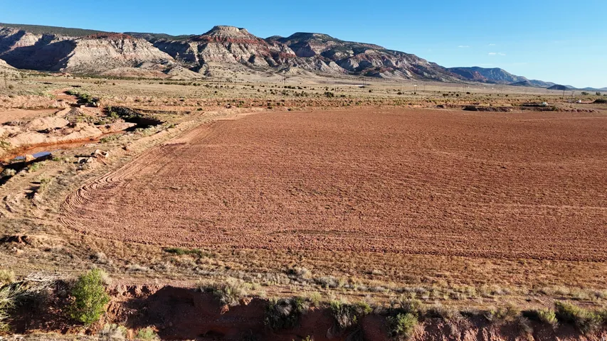 Expansive tilled land with a natural waterway, surrounded by varied terrain and distant mountains