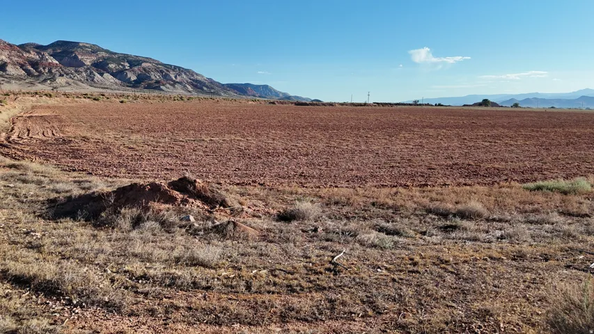 Expansive open land with tilled soil, surrounded by natural vegetation and distant mountains