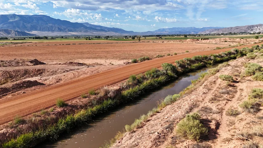 Expansive land parcel featuring a dirt road, natural water channel, and distant mountain range