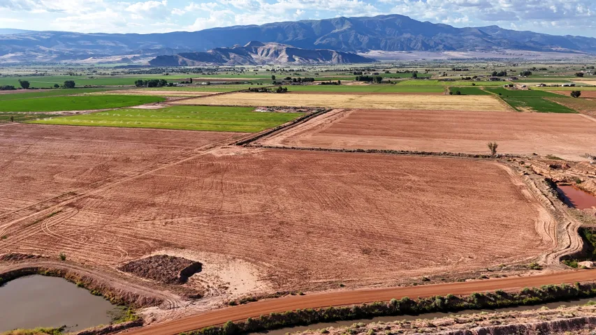Expansive agricultural land featuring cultivated fields, a tranquil pond, and a mountainous backdrop