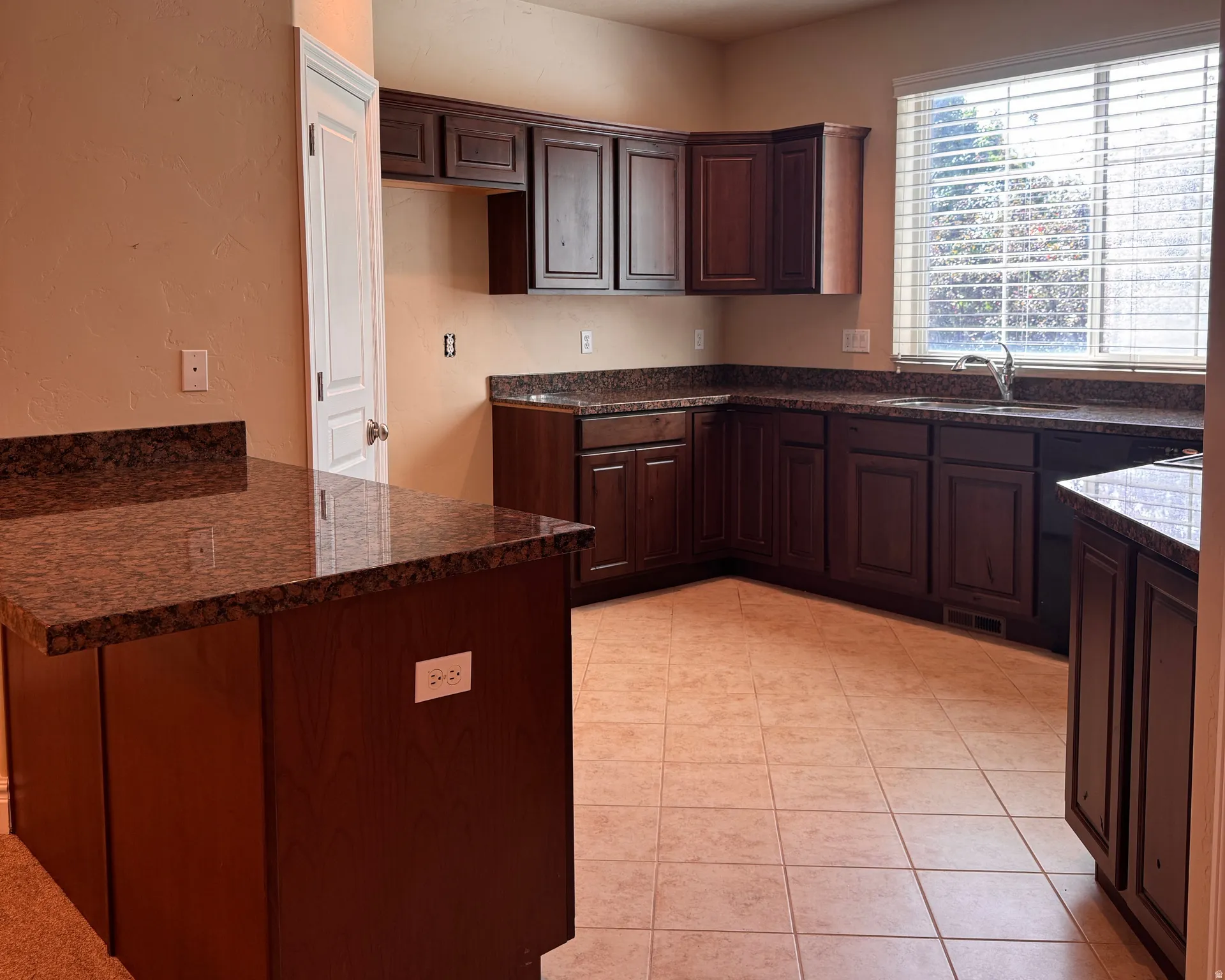Kitchen featuring dark wood-finish cabinetry, granite-style countertops, an undermount sink, a large window, and tile flooring