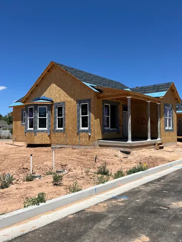 New construction with an unfinished exterior, featuring a bay window, covered front porch with columns, and a newly paved street with a concrete curb