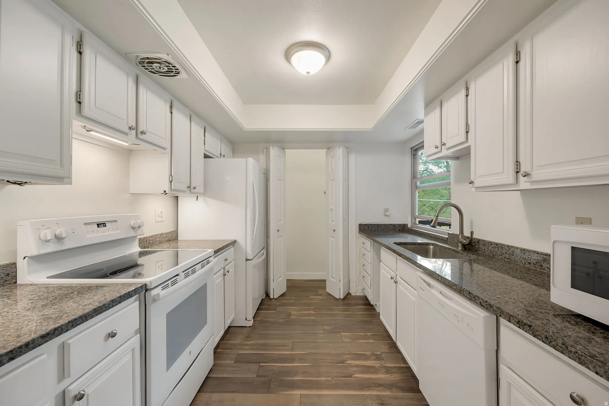 Galley kitchen with white cabinetry. Granite Countertops. Pantry.