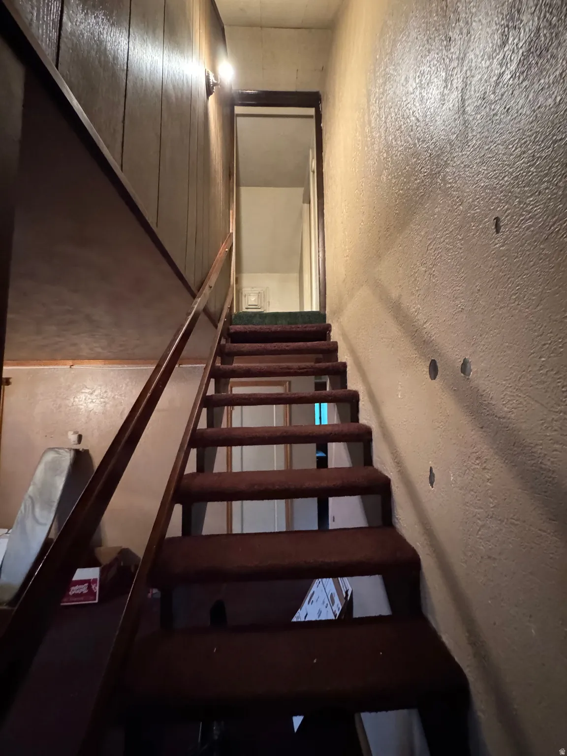 Staircase featuring dark carpeted treads and risers, wooden handrail, and textured wall finish