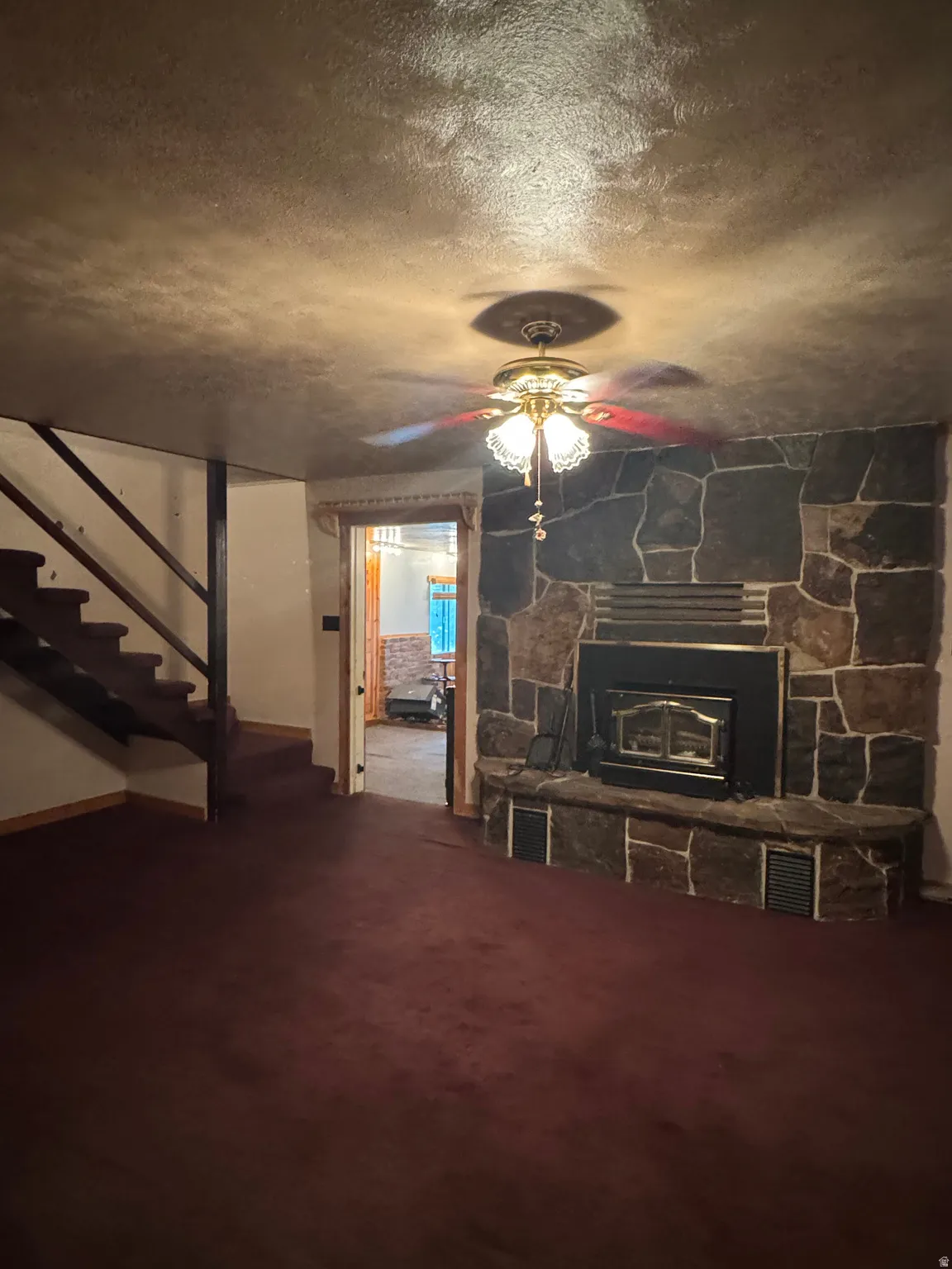 Stone-clad fireplace with a built-in firebox, ceiling fan with integrated lighting, staircase with carpeted treads, and wall-to-wall carpeting