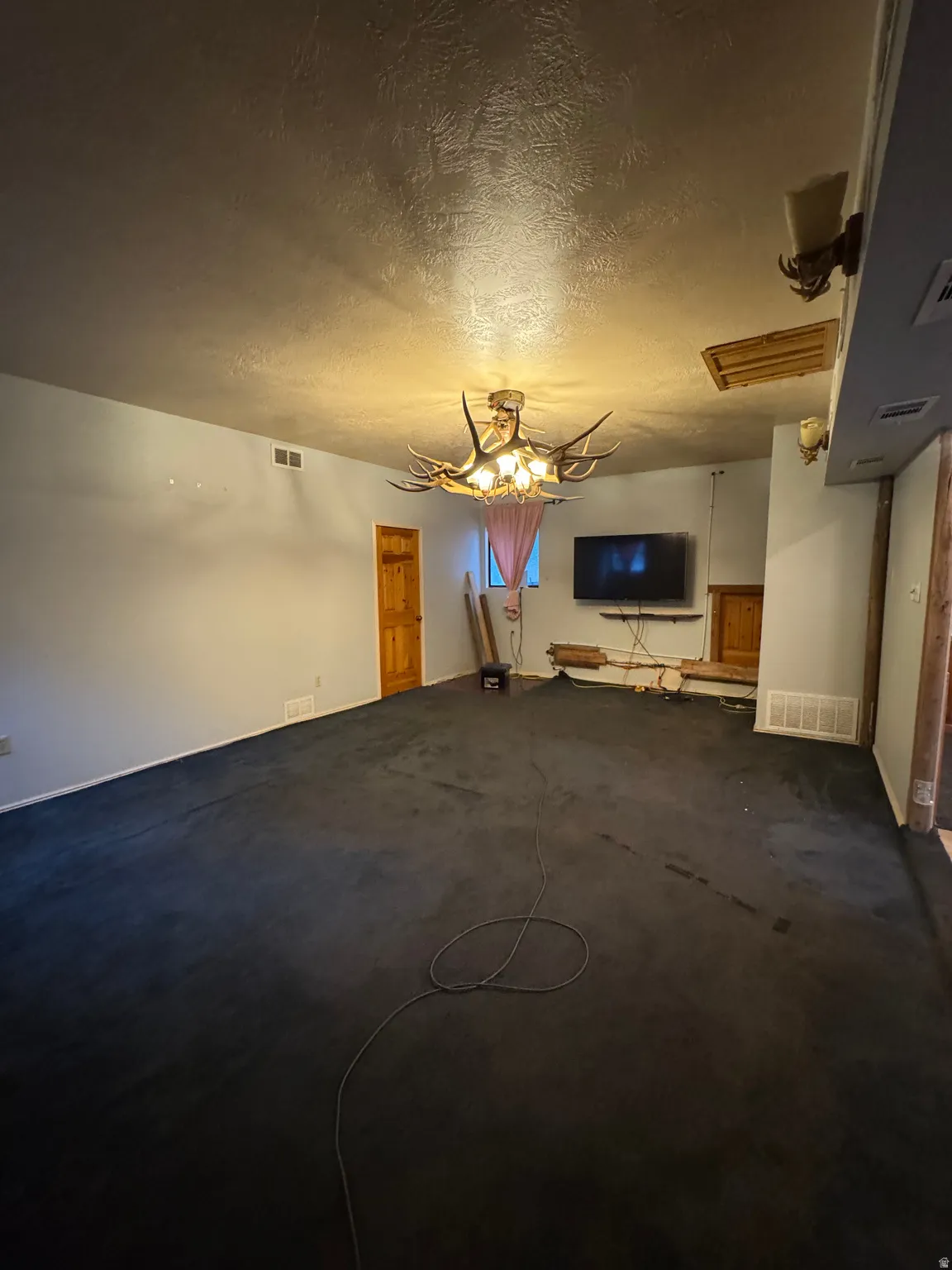 Spacious room with dark carpeting, textured ceiling, and a unique antler-style chandelier