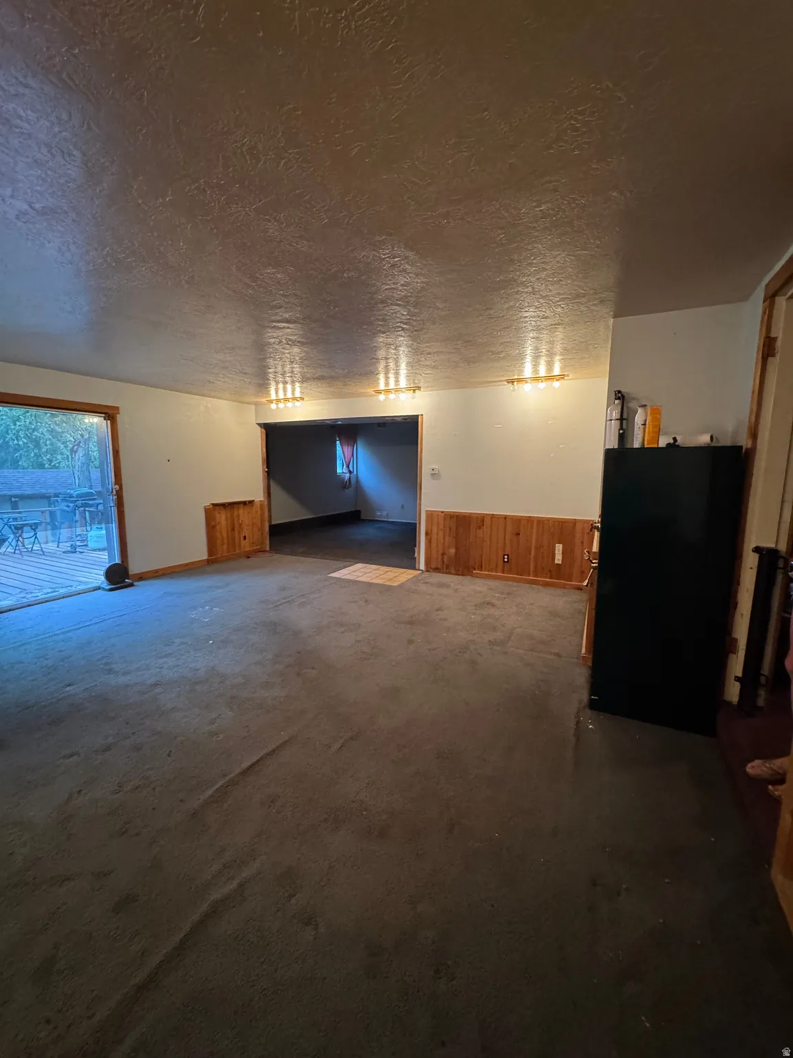Spacious interior room with carpet flooring, wood paneling, and multiple wall-mounted light fixtures