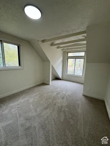 Room featuring exposed ceiling beams, carpeted flooring, two sliding windows, and a flush-mount overhead light fixture