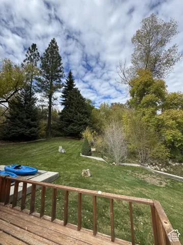 Expansive backyard featuring a wood-railed deck, tiered concrete retaining walls, and mature evergreen and deciduous trees