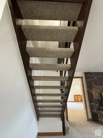Open-riser staircase with dark wood-finish stringers and carpeted treads, complemented by a floor-to-ceiling natural stone fireplace