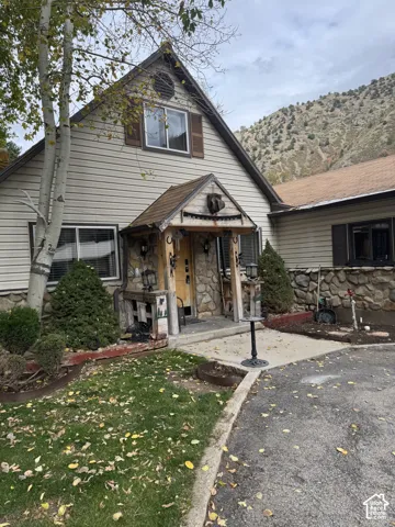 Exterior featuring light-toned horizontal siding, fieldstone accents, a covered front entry with timber supports, and a mountainous backdrop