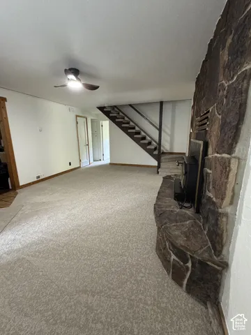 Floor-to-ceiling natural stone fireplace with a raised hearth, wood-frame staircase with open risers, and a ceiling-mounted light fixture with fan