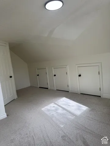Sloped ceiling room featuring wall-to-wall carpeting, three built-in access doors, one full-height door, and a circular flush-mount ceiling light
