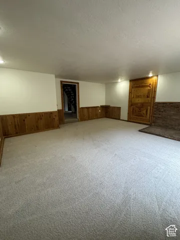 Interior space featuring wood wainscoting, recessed lighting, carpeted flooring, and a decorative brick fireplace surround with a wooden door panel