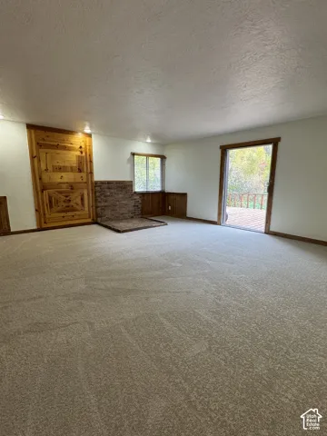 Living area featuring textured walls, neutral carpeting, a brick hearth, custom wood-paneled accents, and a sliding glass door providing exterior access