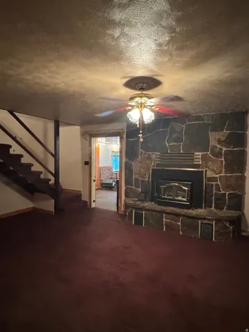Stone-clad fireplace with a built-in firebox, ceiling fan with integrated lighting, staircase with carpeted treads, and wall-to-wall carpeting