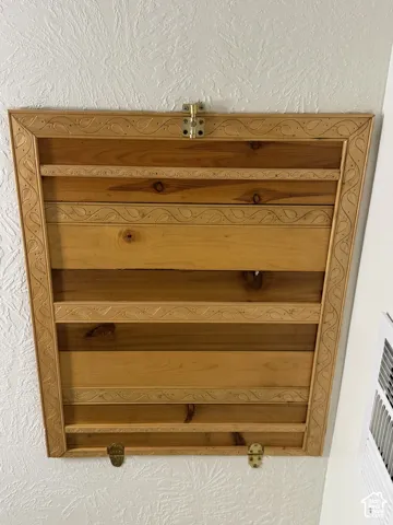 Wall-mounted wooden cabinet featuring natural wood grain, intricate carved border detailing, and brass-finish hardware