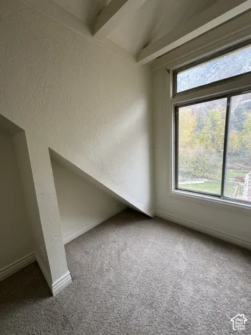 Vaulted ceiling featuring exposed beam detail, carpeted flooring, and a large window with mountain and landscape scenery
